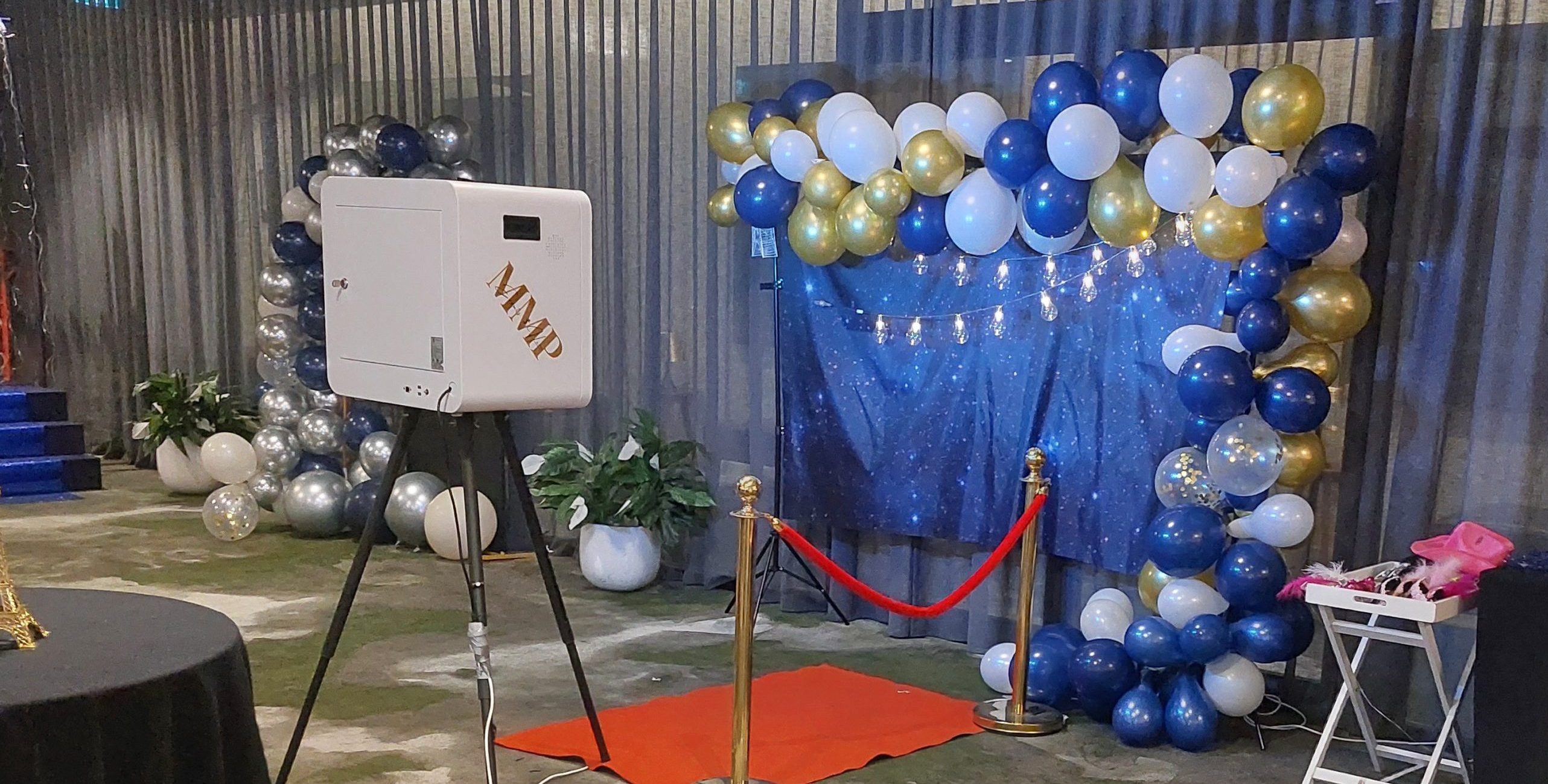Memories Made and Personalised - Memories Made and Personalised - Balloon Arch in Blue, White, and Gold with a Glittery Blue Backdrop, Red Rope Barrier, and a Photo Booth Machine on a Tripod Nearby in an Event Space. -  - Photo Booth Hire | Packages & Pricing | Mmp Events -  - Photo Booth Hire | Packages & Pricing | Mmp Events